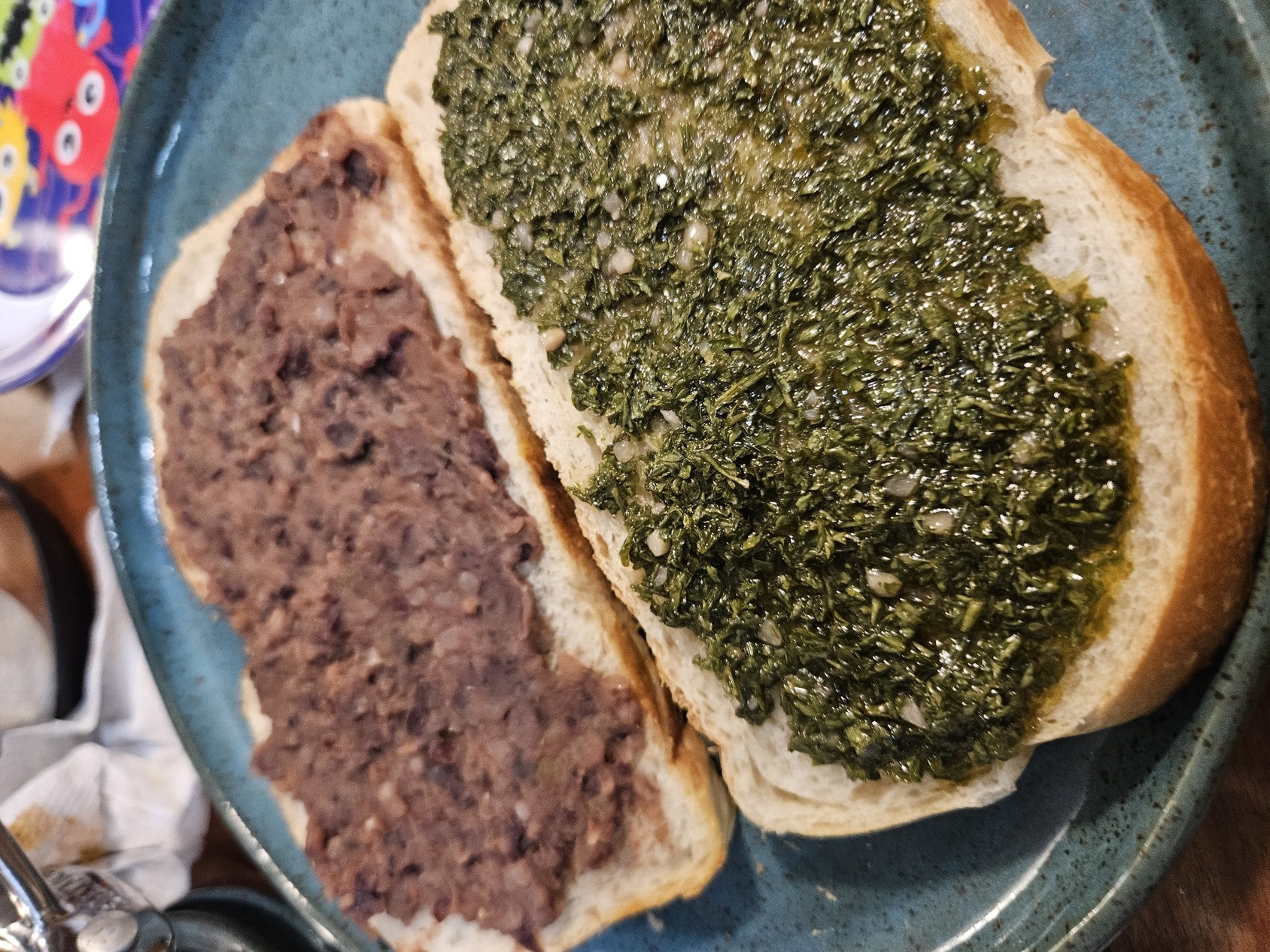 A picture of two slices of bread covered in bean paste and chimichurri