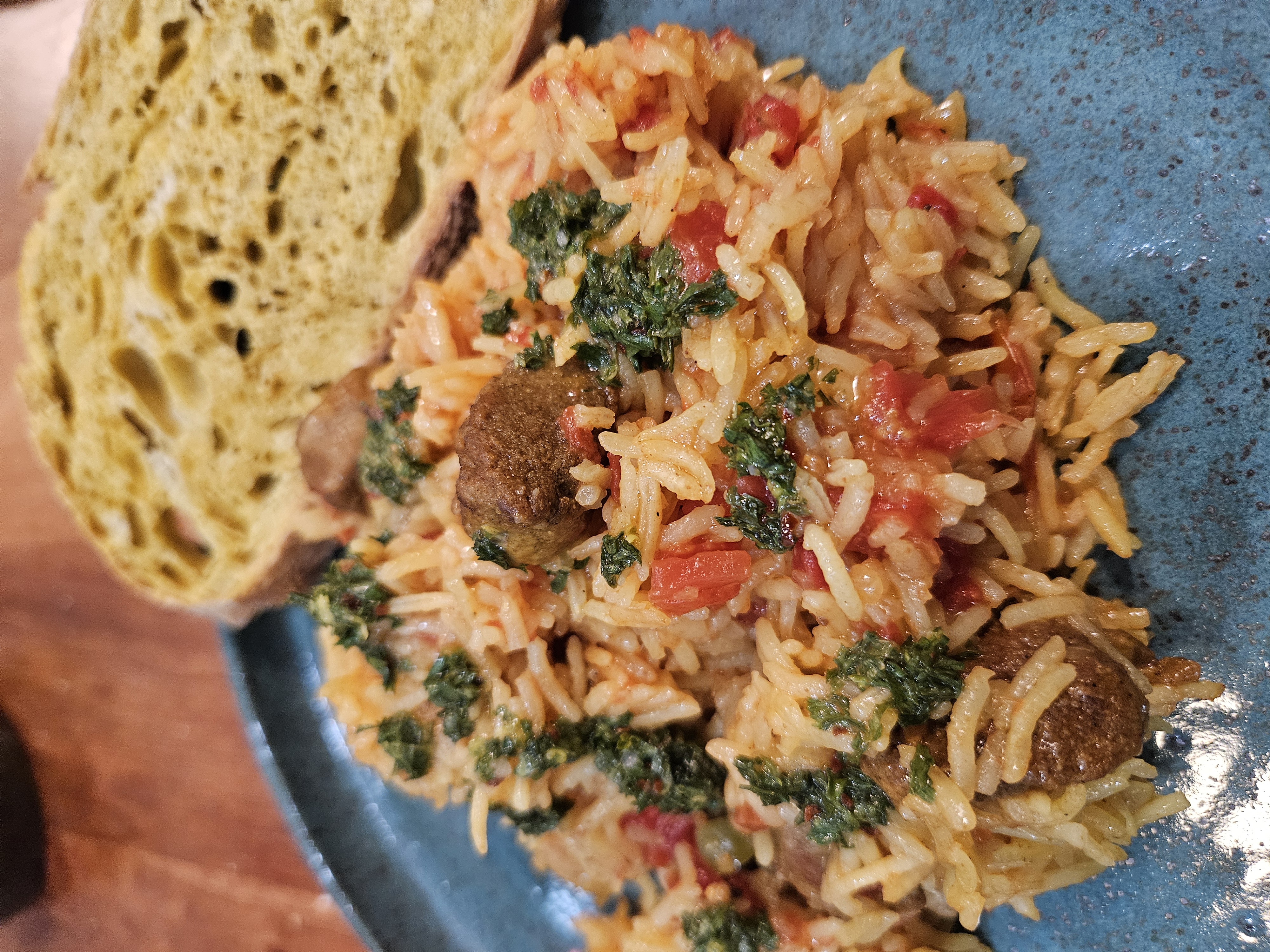 A green plate with yellow rice, dotted by tomatoes and green herb sauce